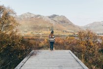 Back view of woman standing on wooden pier at lake in mountains. — Stock Photo