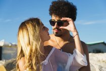 Menina jovem sobre ombro ajustando óculos de sol no namorado elegante — Fotografia de Stock