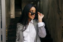Stylish woman wearing jacket putting on sunglasses — Stock Photo