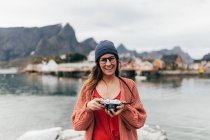 Mujer morena sonriente en gafas posando con cámara en el muelle del lago - foto de stock