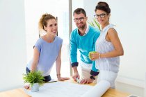 Group of business people standing at table with big paper sheet and looking at camera in modern office. — Stock Photo