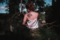 Visão traseira da morena com tatuagem nas costas cutucando na floresta — Fotografia de Stock