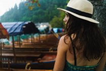 Visão traseira da mulher morena usando chapéu posando perto de barcos — Fotografia de Stock
