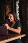 Ritratto di bruna sorridente seduta al tavolo del caffè con laptop e smartphone di navigazione — Foto stock