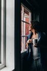 Femme avec tasse regardant dans la fenêtre — Photo de stock