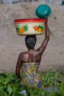 BENIN, ÁFRICA - 30 de agosto de 2017: Vista trasera de una mujer africana en un estanque sosteniendo un tazón grande en la cabeza . - foto de stock