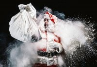 Shouting Santa Claus holding sack over snow explosions — Stock Photo