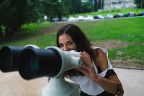 Mulher morena alegre segurando sightseeing máquina binocular e olhando para a câmera — Fotografia de Stock
