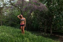 Deportiva chica posando en el césped junto a púrpura árbol en flor - foto de stock