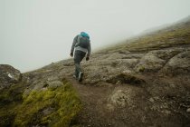 Visão traseira do homem que caminha acima da inclinação rochosa do musgo-coberta da colina — Fotografia de Stock