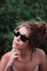 Портрет юной брюнетки в черных солнцезащитных очках и позирующей на камеру . — стоковое фото