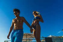 Vista ad alto angolo della coppia in occhiali da sole che cammina sulla spiaggia illuminata dal sole — Foto stock