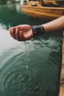 Обрізати жіночу руку зі шкіряним браслетом, взявши воду з озера — стокове фото