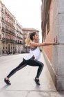 Seitenansicht einer sportlichen Frau, die sich mit den Händen an die Wand lehnt und ihren Körper streckt — Stockfoto