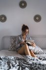 Porträt eines brünetten Mädchens, das im Hemd auf dem Bett sitzt und Buch liest — Stockfoto