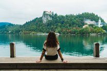 Vue arrière de la femme brune assise sur la jetée et regardant les collines sur le lac — Photo de stock