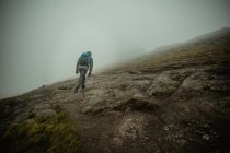 Rear view of man wearing backpack walking up foggy green slope of hill — Stock Photo