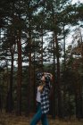 Vista lateral da menina morena em camisa quadriculada andando na floresta e olhando para cima . — Fotografia de Stock