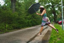 Vista laterale della donna con ombrello che salta sopra la pagaia su strada — Foto stock