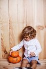 Criança encantadora posando com abóboras por parede de madeira — Fotografia de Stock