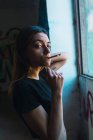 Portrait of brunette looking at camera while smoking at window in abandoned building. — Stock Photo