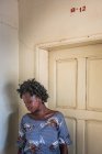 BENIN, AFRICA - AUGUST 31, 2017: Pensive black woman standing at white door and looking down. — Stock Photo