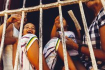 CUBA - AUGUST 27, 2016: Cheerful kids and adults standing behind metal bars at street scene — Stock Photo