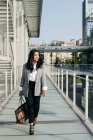Empresária sorridente elegante andando na passagem da varanda e olhando para longe — Fotografia de Stock