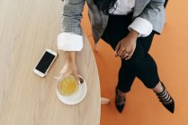 Imagem de corte de mãos de mulher segurando xícara de chá na mesa com smartphone — Fotografia de Stock