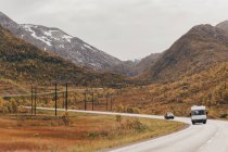 View to cars driving through mountains on asphalt road in cloudy day. — Stock Photo