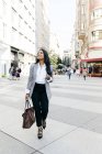 Элегантная женщина с сумочкой ходит по улице и смотрит в сторону — стоковое фото