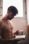 Mann hält Tasse und liest Buch zu Hause — Stockfoto
