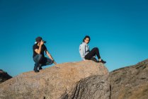 Vue latérale du photographe prenant une photo de fille assise sur le bord du rocher — Photo de stock