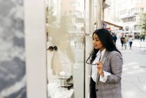 Стильная женщина в очках с интересом смотрит в витрину магазина — стоковое фото