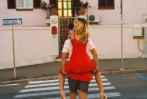 Мужчина несет молодую девушку на спине и переходит дорогу — стоковое фото