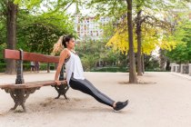 Side view of sporty girl doing exercise on park bench — Stock Photo