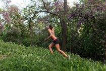 Вид сбоку на спортивную девушку, бегущую по холму в парке — стоковое фото
