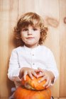 Blond child boy posing with pumpkin by wooden wall — Stock Photo