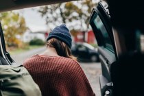 Visão traseira da mulher no jumper de malha e chapéu saindo do carro — Fotografia de Stock