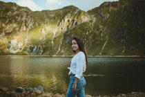 Smiling pretty woman standing in lake in hillside and touching hair. — Stock Photo