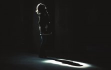 Anonyme Frau steht im Scheinwerferlicht von oben in dunklem Raum. — Stockfoto