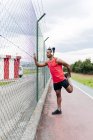 Вид сбоку спортсмена, опирающегося на забор и растягивающего ногу перед тренировкой — стоковое фото