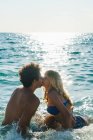 Loving couple kissing in blue ocean waves in bright back light. — Stock Photo