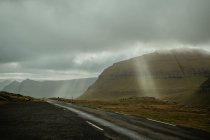 Sunbeams penetrating clouds over highlands countryside road — Stock Photo