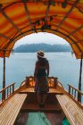 Rückansicht einer brünetten Frau, die auf einem Boot am See posiert und zur Seite schaut — Stockfoto
