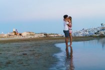 Vista lateral distante de casal amoroso abraçando na praia — Fotografia de Stock