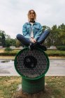 Jeune femme assise avec les jambes croisées sur un tube de ventilation au parc — Photo de stock