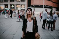 Женщина с камерой в руках стоит на городской улице и смотрит вверх — стоковое фото