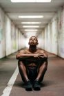 Спортсмен без рубашки сидит на полу в подземном переходе и смотрит вверх — стоковое фото