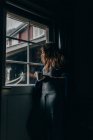 Низкий угол зрения женщины с кружкой, смотрящей в окно — стоковое фото